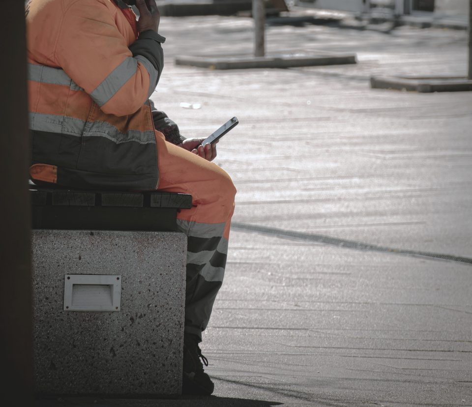 Person i vernetøy sitter på en benk og bruker mobiltelefon